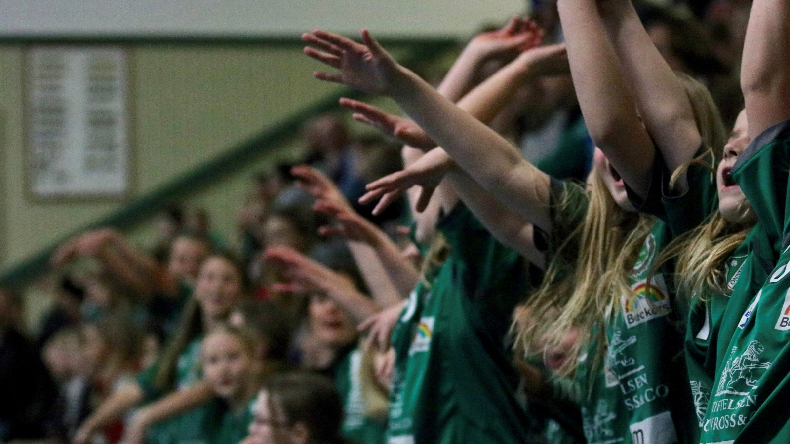 unga tjejer i publiken på en handbollsmatch som hejar och håller händerna upp i luften